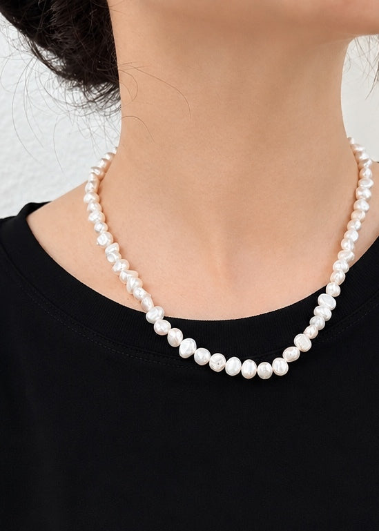 A close-up of a model wearing a classic strand of white freshwater pearl necklace with a black top.
